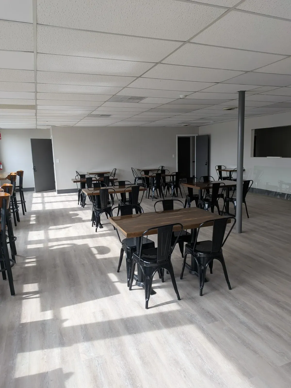 Wide view of the MC² workspace with window bar seating, café tables and a wall-mounted screen